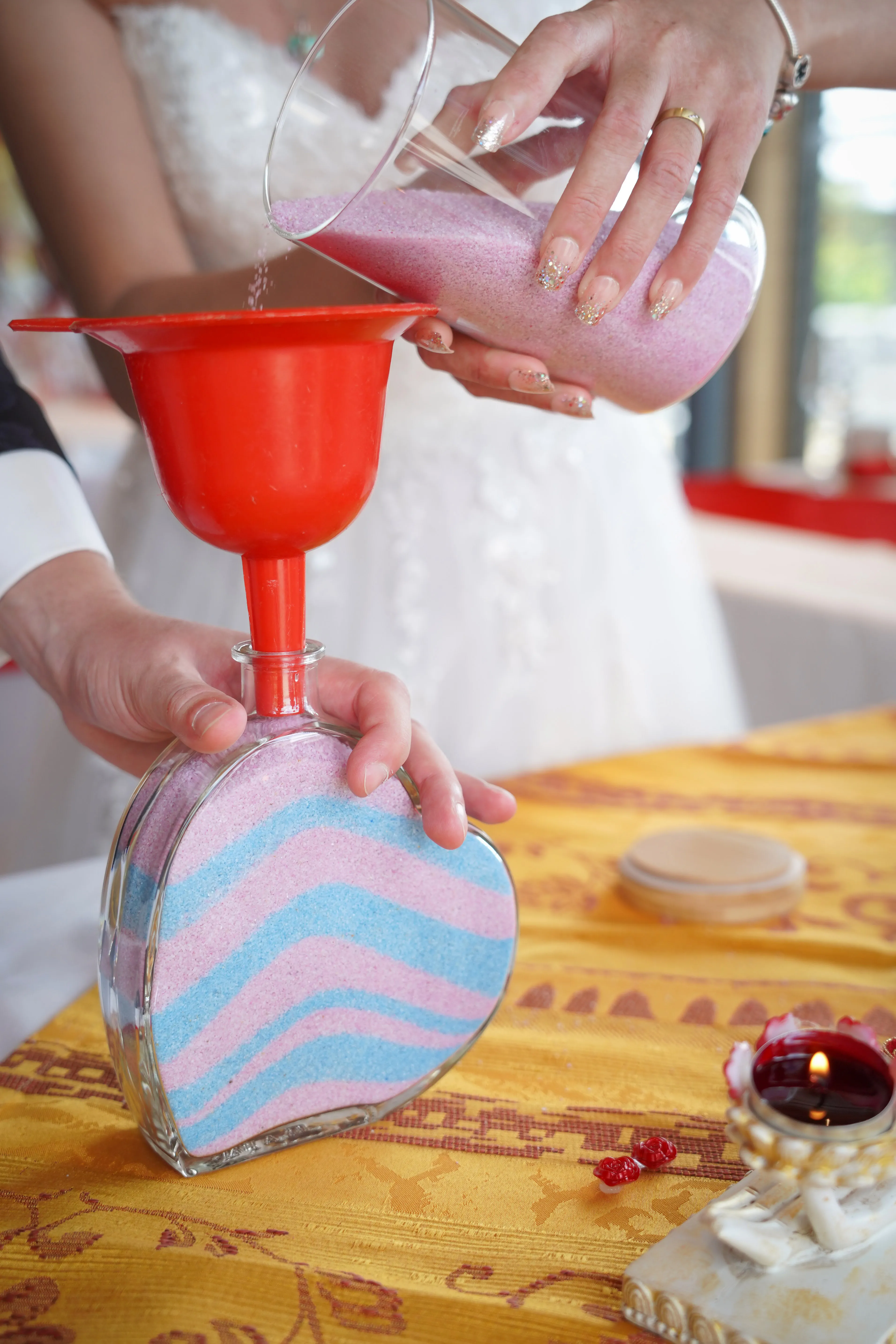 Herzförmige Vase wird beim Sandritual per Trichter mit rosa und blauem Sand gefüllt
