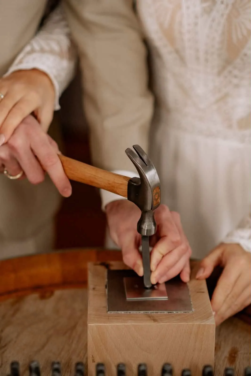 Brautpaar hämmert Hand in Hand gemeinsam das erste Wort in die Metallplatte beim Wortschmiede-Ritual