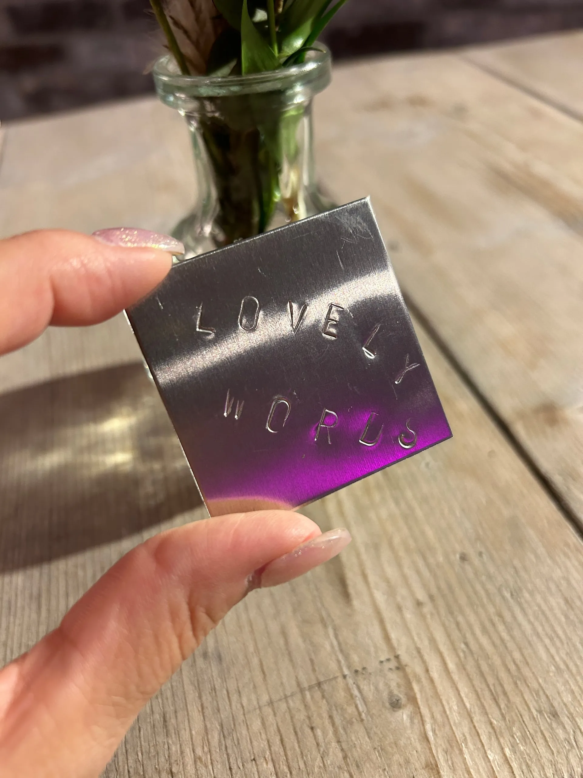 Fertig geprägtes Metallplättchen mit dem Wort „Lovely Words“ als bleibendes Andenken beim Wortschmiede-Ritual