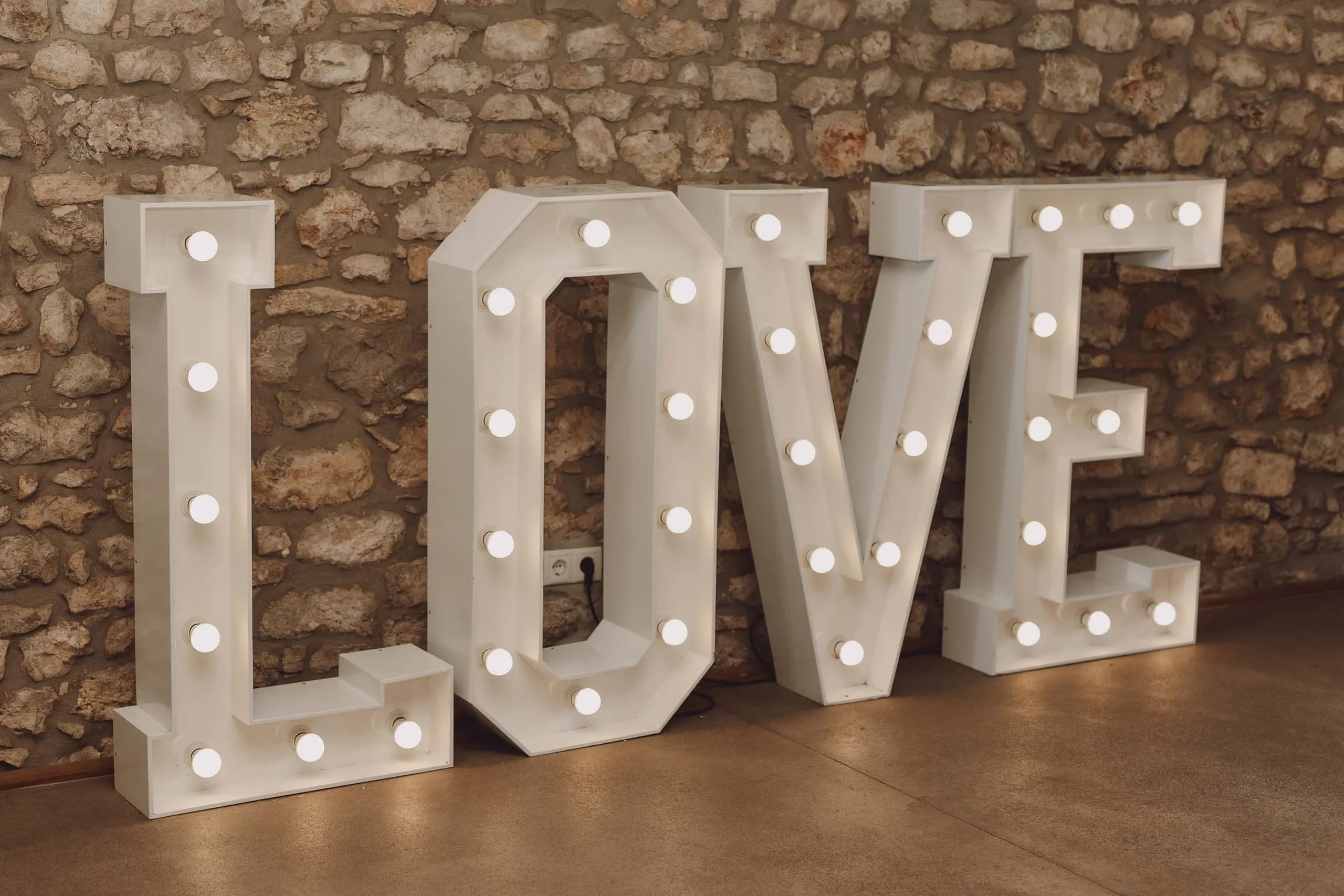 LOVE Leuchtbuchstaben vor rustikaler Natursteinmauer bei einer Hochzeit