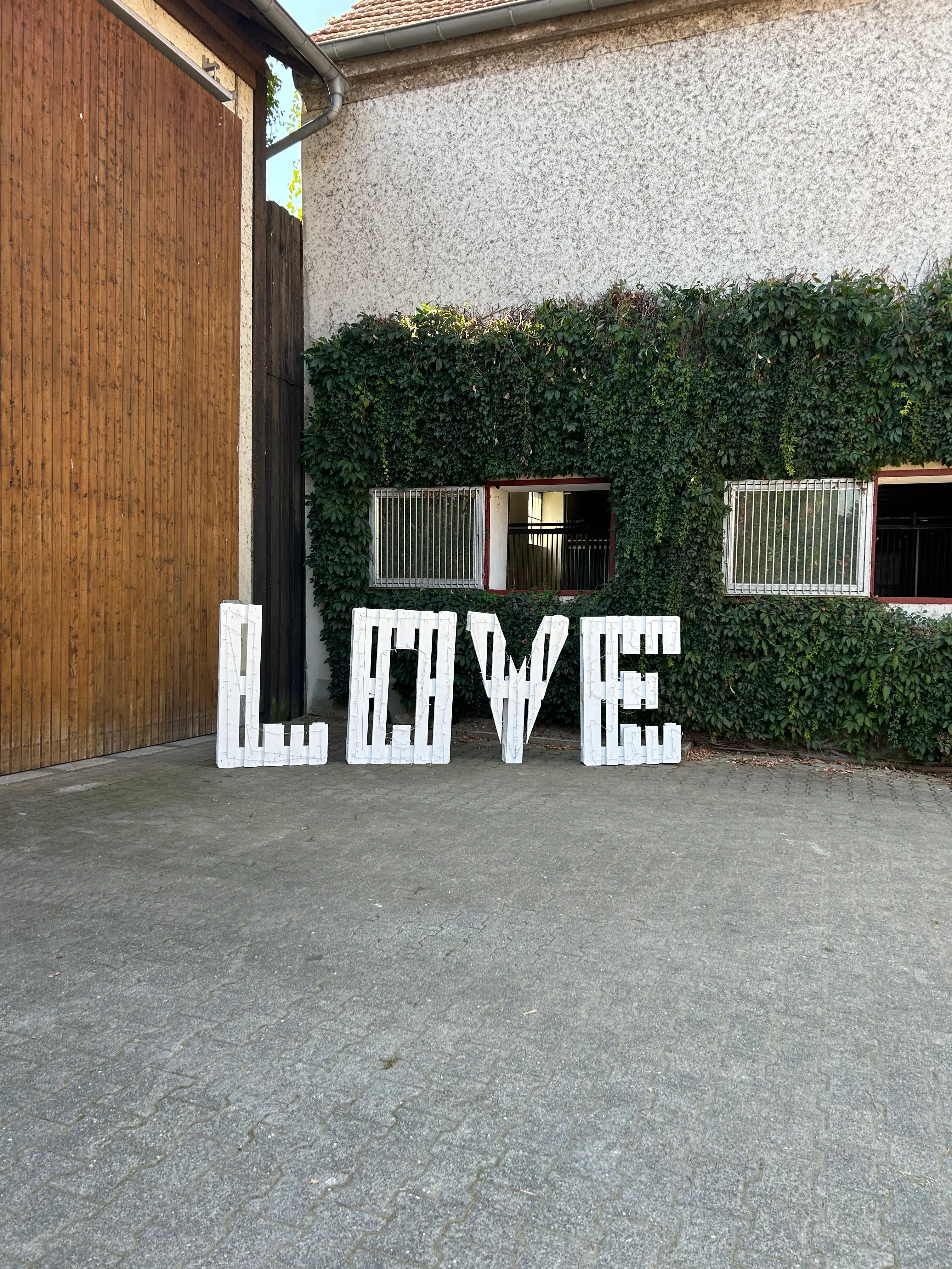 LOVE-Buchstaben auf einer Holzterrasse vor grüner Hecke
