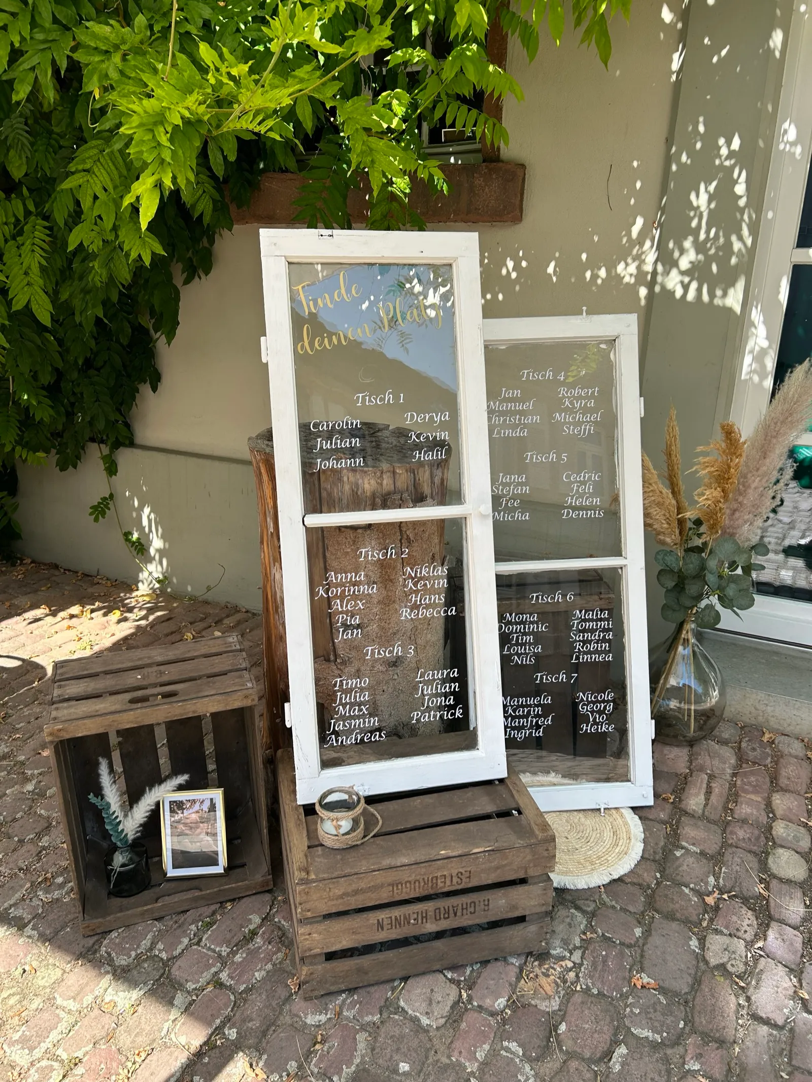 Vintage-Sitzplan aus alten Fensterscheiben mit goldener Schrift auf Holzkisten