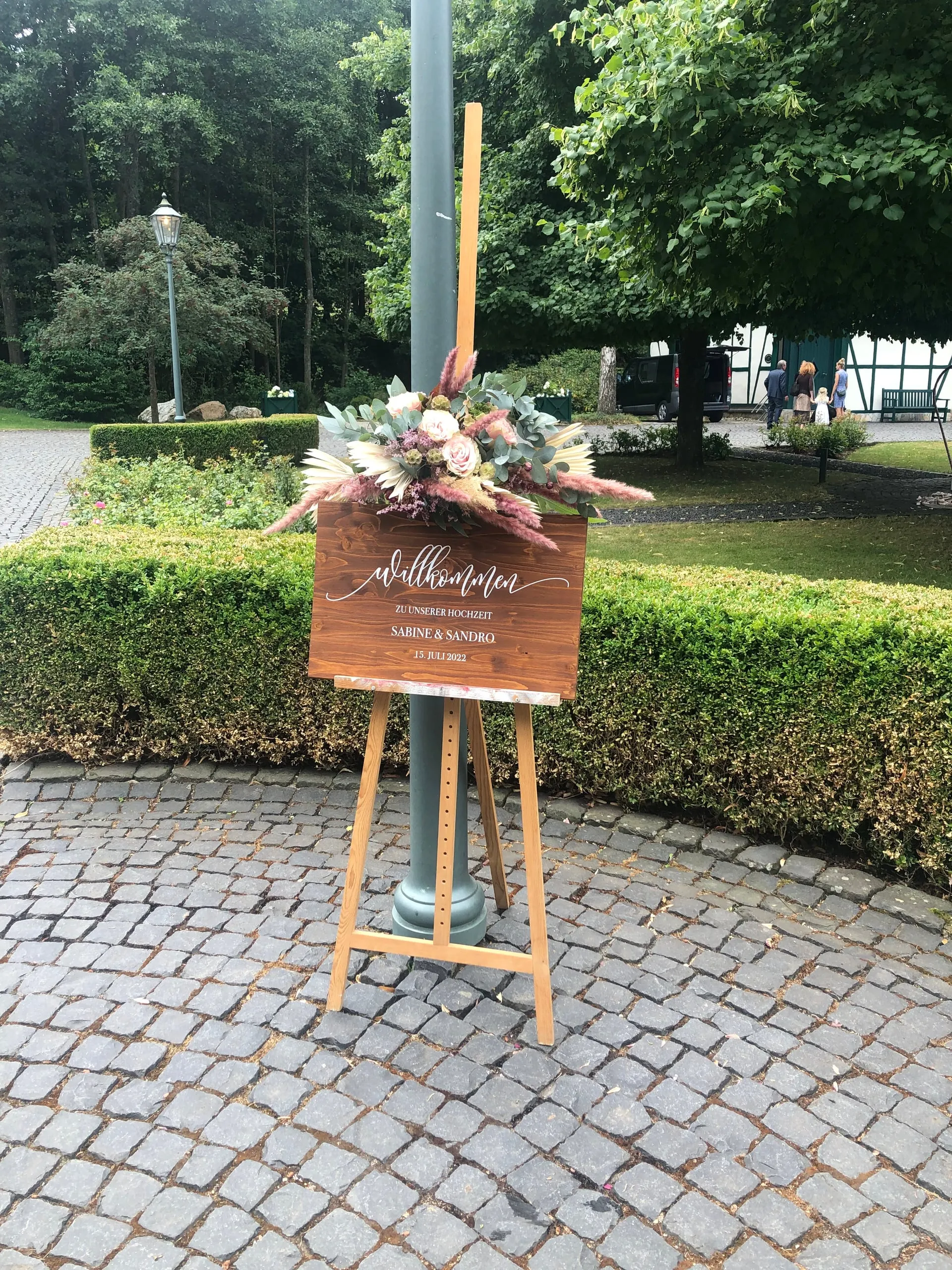 Willkommensschild aus Holz mit Blumenarrangement auf einer Staffelei bei einer freien Trauung