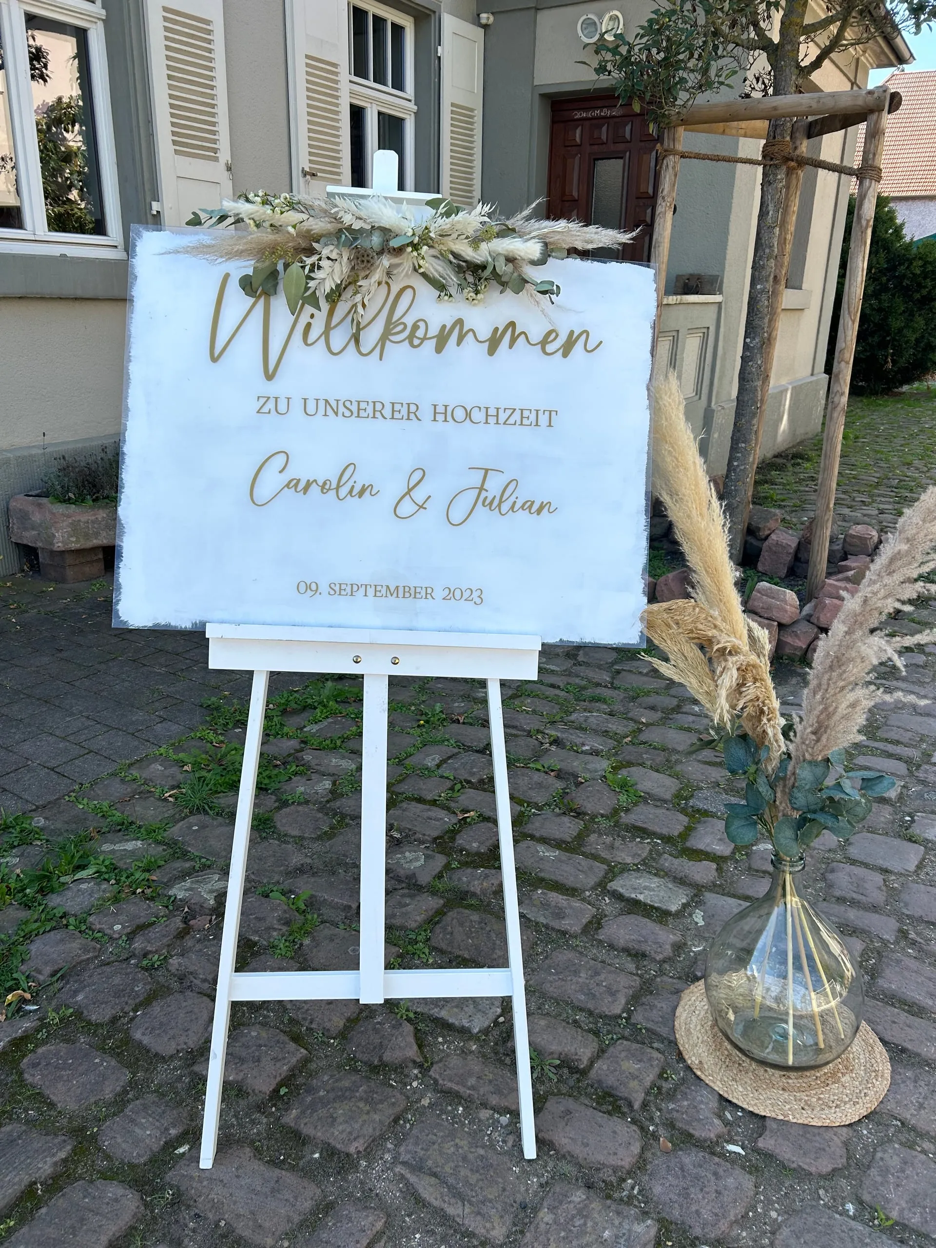 Elegantes weißes Willkommensschild mit goldener Kalligrafie auf weißer Staffelei